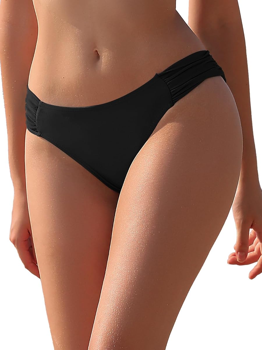 Bas de bikini noir uni à coupe brésilienne posé sur une pierre claire près d’un lin ivoire.