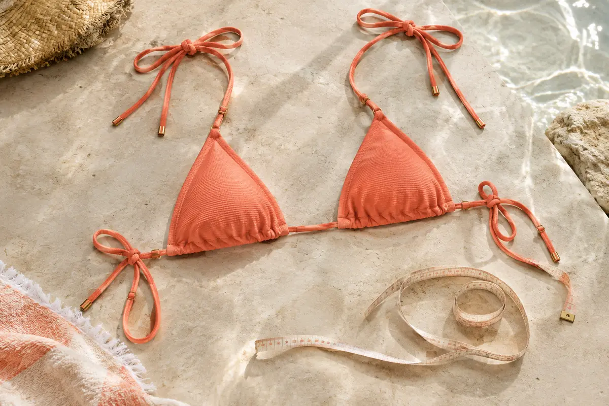 Haut de bikini triangle posé à plat avec un mètre ruban souple pour préparer la prise de mesures